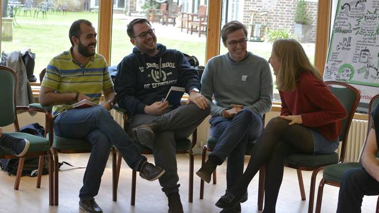 Four LSE students, three women and a man, sitting down chatting and laughing together on the Faith and Leadership residential