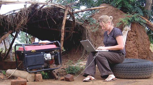 Woman sitting on a tyre works on a laptop in a makeshift camp