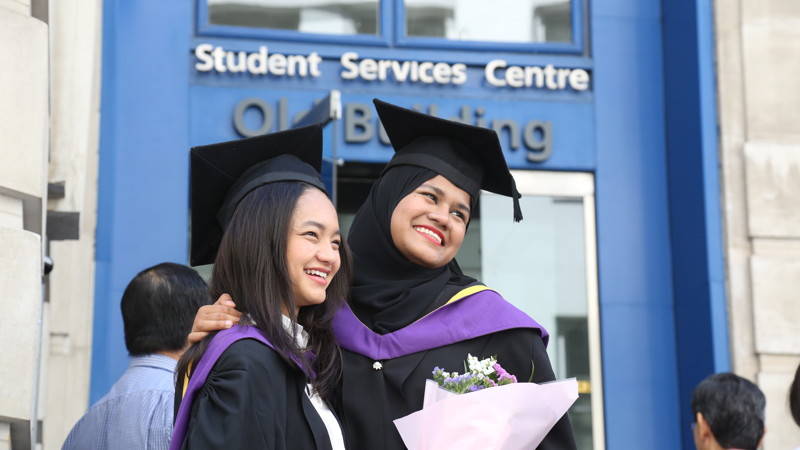 Two graduands posing outside the Old Building