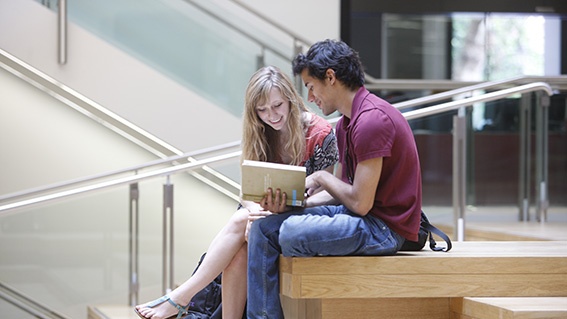 Two students looking at a book in the NAB atrium
