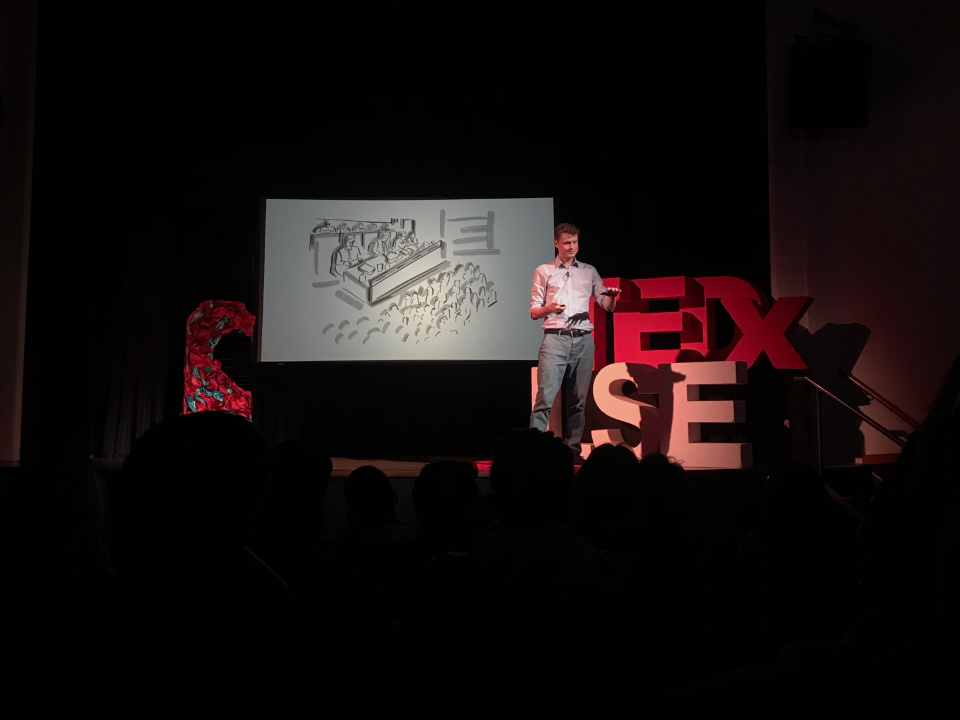 A man presenting on stage at the annual TEDxLSE talk 2019