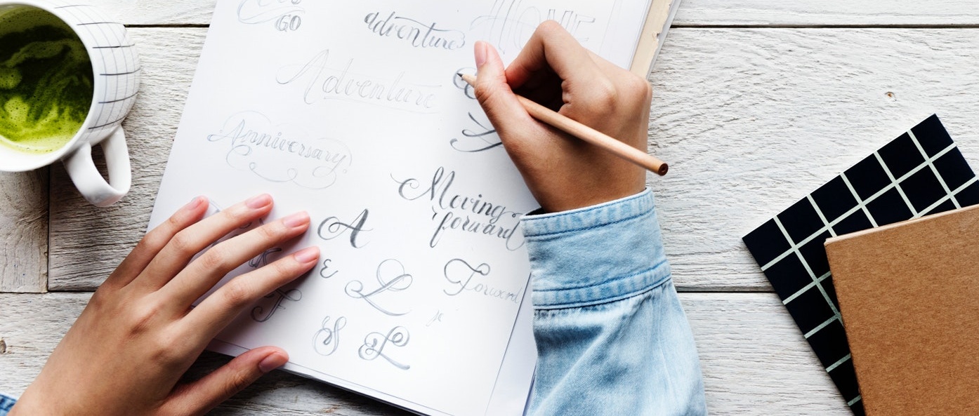 A person writing with a pencil on a notepad.