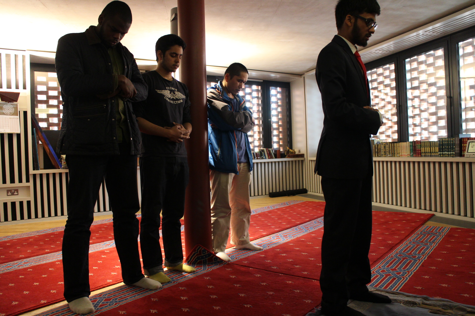 Four male Muslim students standing to pray in the prayer room