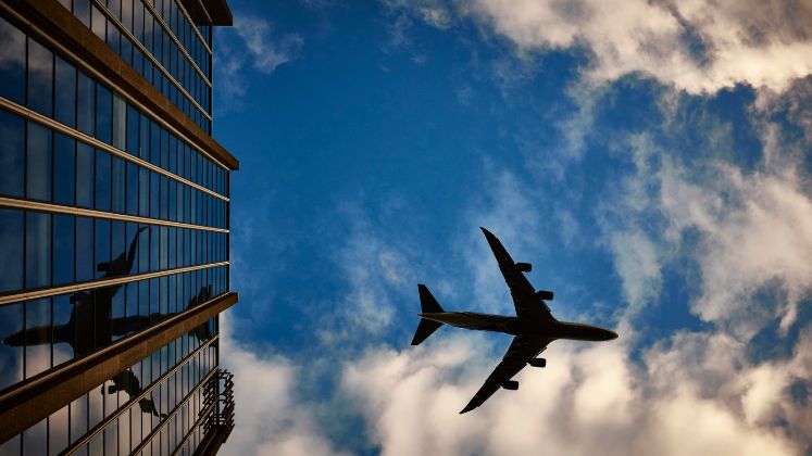 An aeroplane flying across a blue sky above buildings