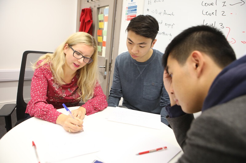 a teacher advising two students at a table whilst drawing