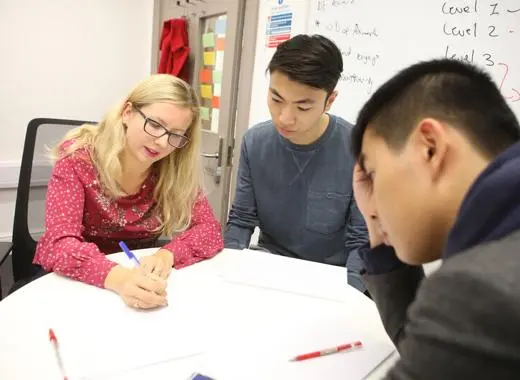 a teacher advising two students at a table whilst drawing