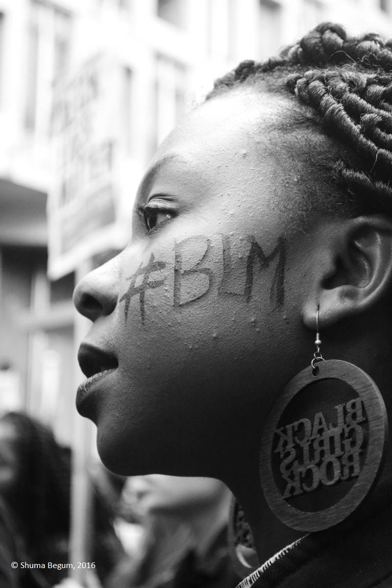 Photo taken by Shuma Begum of a woman at a Black Lives Matter protest with #BLM written on her cheek