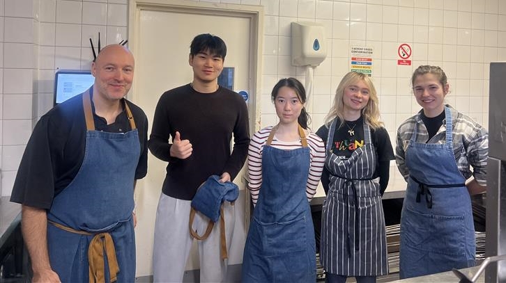 A group of people standing in a kitchen, wearing aprons