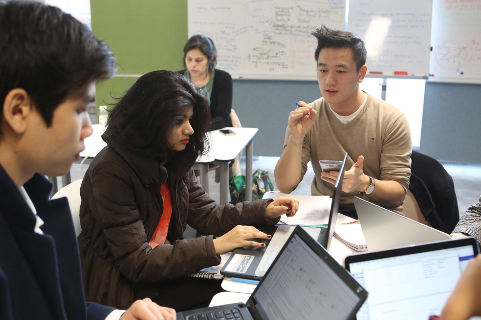 Students are sat at a table together, discussing an assignment