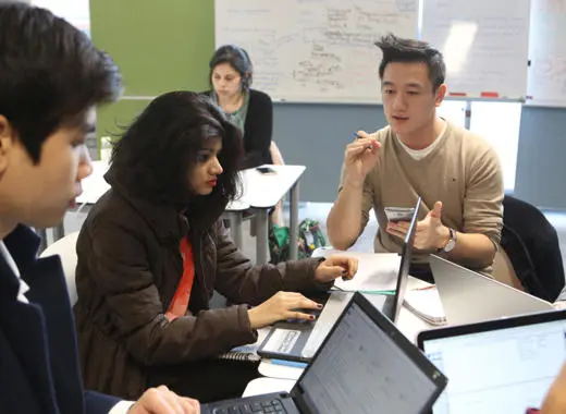 Students are sat at a table together, discussing an assignment