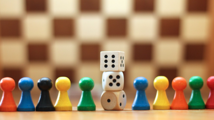 A chess boardin the background with dice and coloured figurines in the foreground