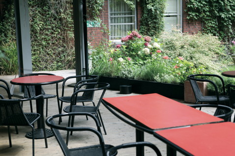 Red tables and black chairs outside with green plants in the background